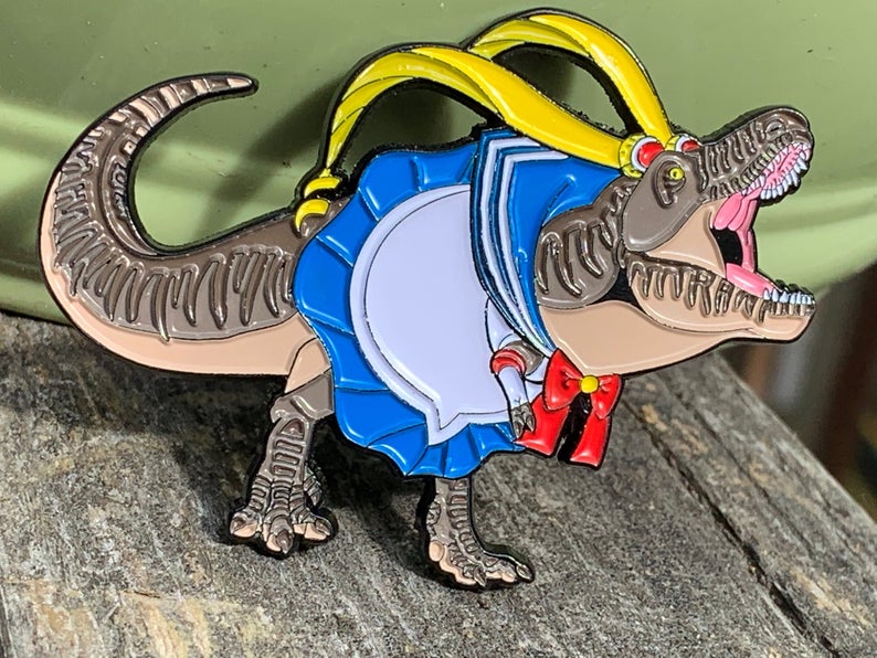 Enamel pin design of a T. rex wearing a Sailor Moon style outfit